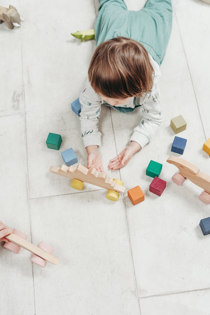 Child playing with colorful wooden toys on a light floor, creating a fun and educational setting.